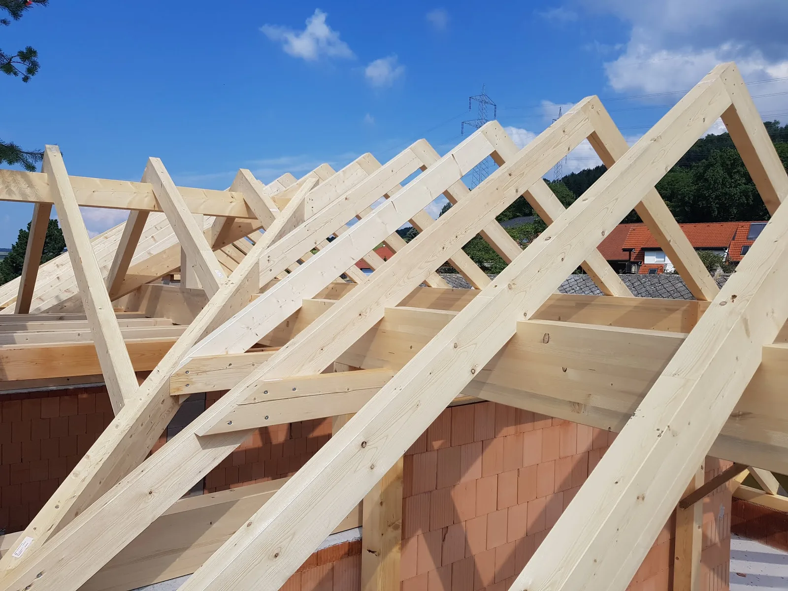 Neuer Dachstuhl aus hellem Nadelholz über Ziegelmauerwerk vor blauem Himmel