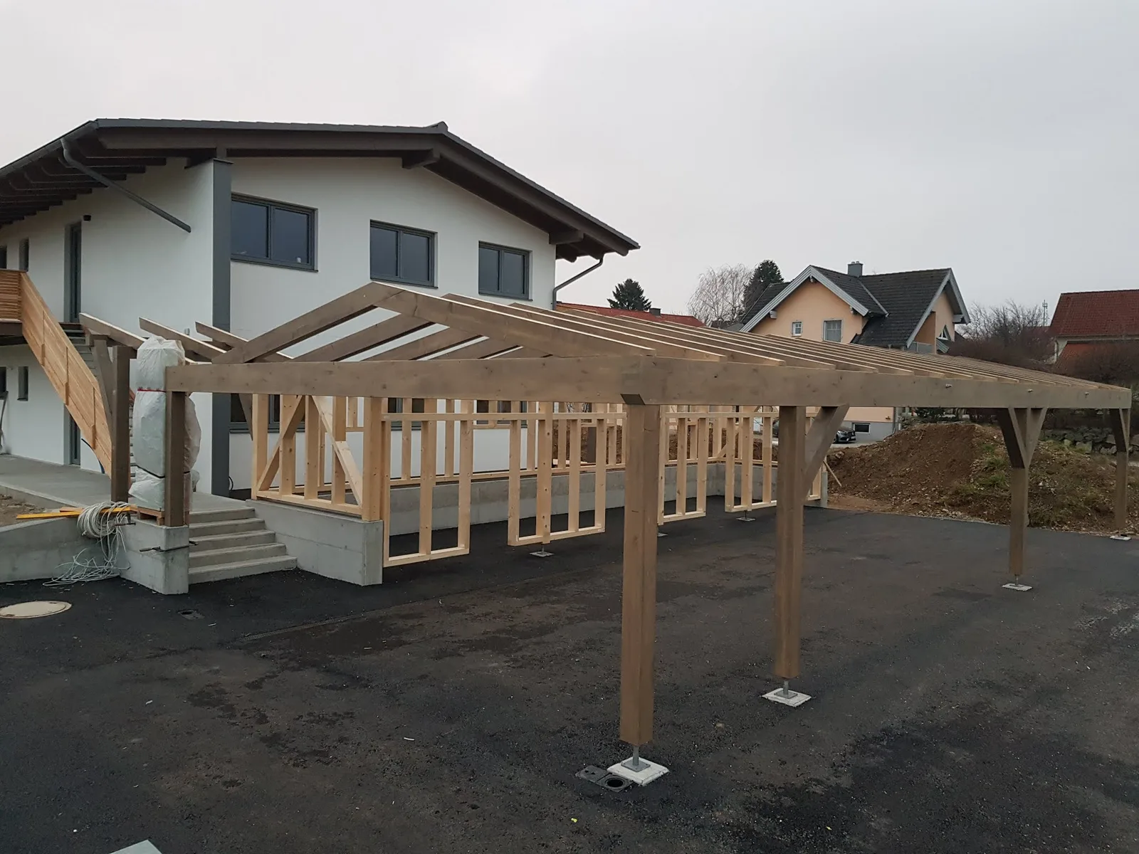 Carport-Tragwerk und Holzriegelwand vor einem fertigen Wohnhaus