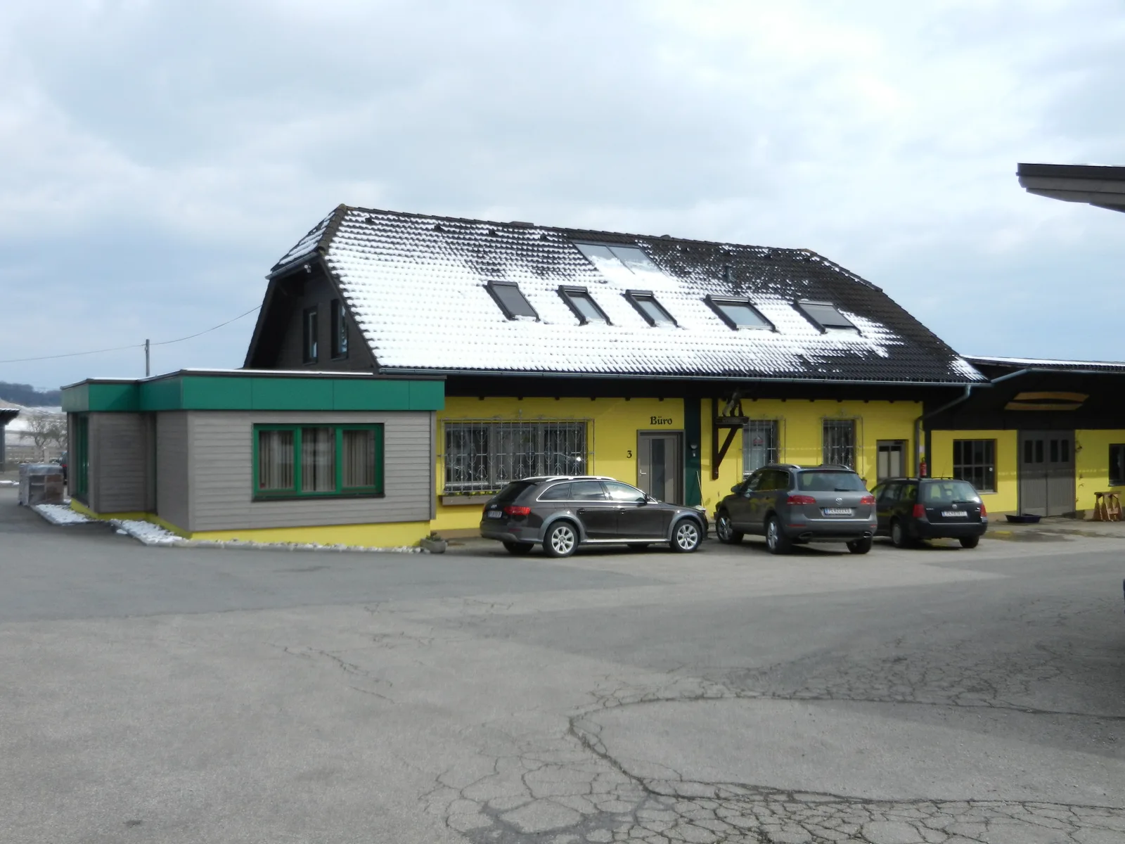 Betriebsgebäude mit gelber Fassade, grünem Vordach und der Aufschrift Büro