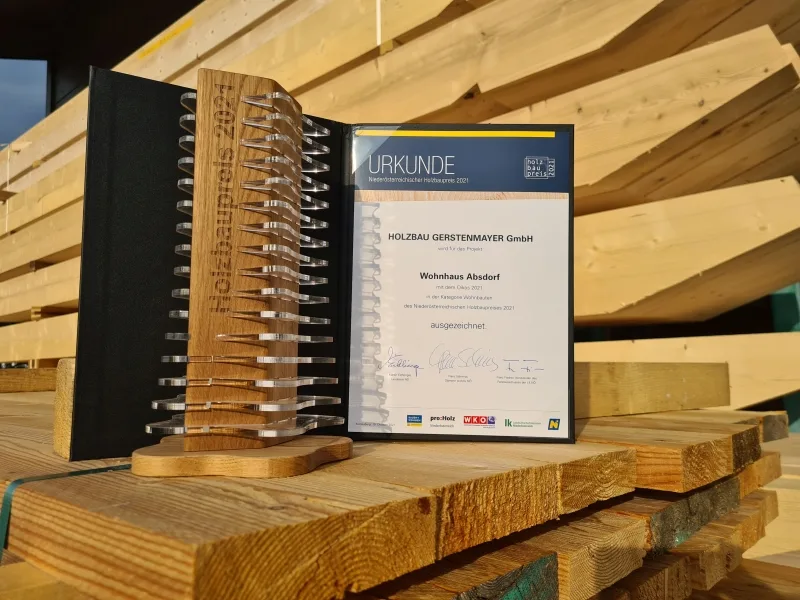 Urkunde des Niederösterreichischen Holzbaupreises für das Wohnhaus Absdorf neben der hölzernen Trophäe